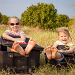 Deux petites filles souriantes, chacune assise dans une valise posée dans l'herbe.